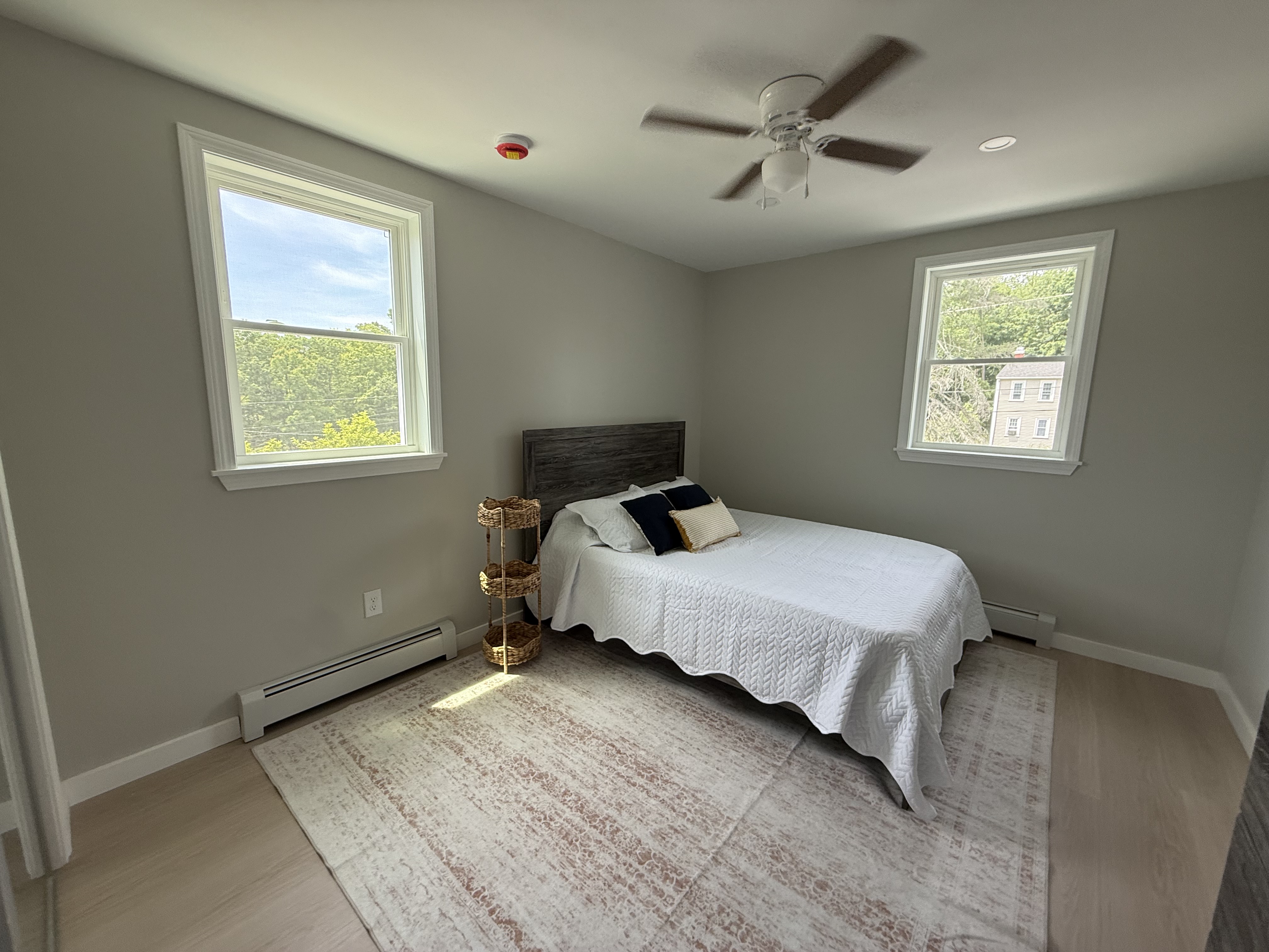 Renovated bedroom with light wood floors, sage walls, and two bright windows
